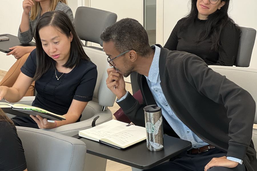 Two people leaning over an open notebook and a tablet, working through something together