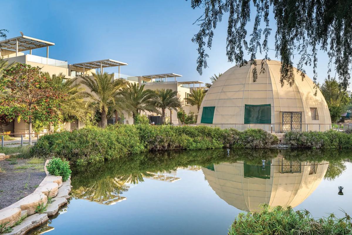 A planted lake in The Sustainable City, Dubai, with a domed biodome reflected in the water